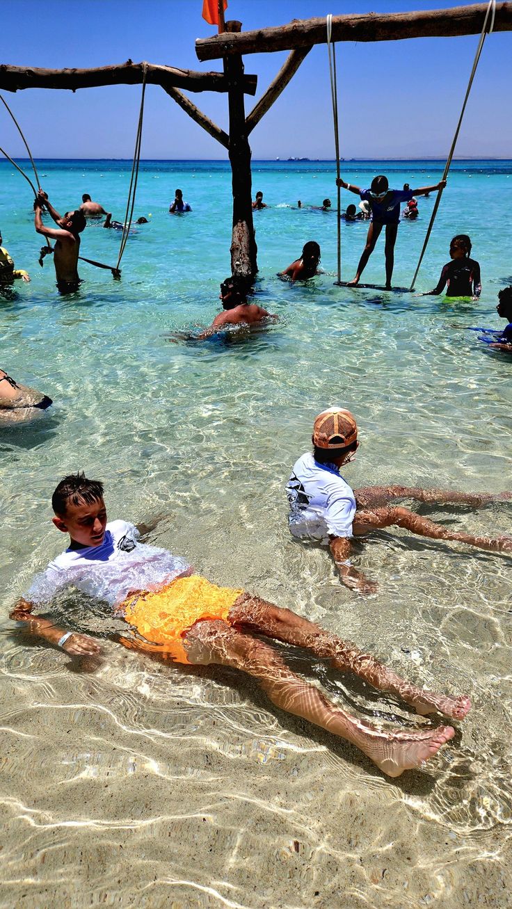 Kids playing in the shallow water next to the sea swings
